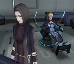 Juli Mizrahi stands looking pensive in front of a computer panel in the maintenance lab on Second Miltia, with her back toward Ziggy, who sits in a chair behind her.