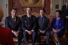 The royal family is sitting on an ornate pink couch. Ludvig and Wilhelm are wearing standard dark suits, whereas Kristina is in a monochrome blue velvet coat, a blue skirt, and a blue blouse. Erik is in what appears to be a Swedish formal military uniform. They are all sitting with their hands clasped in their laps and looking offscreen.