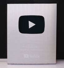 The new version of the Silver Play Button, which doesn't have the frame and is flatter than the original version.