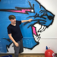 MrBeast next to a wall with his logo painted on it.